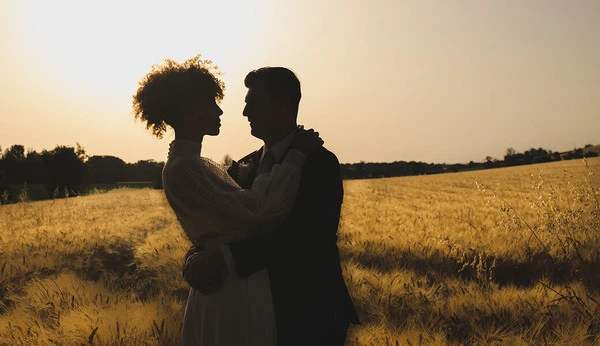 Un couple de mariés s’enlace devant un champ de blé au coucher du soleil en Occitanie Crédit photo : Sophie Bachère