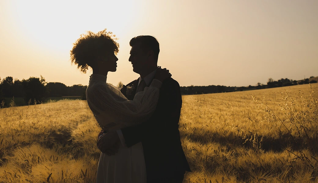 Un couple de mariés s’enlace devant un champ de blé au coucher du soleil en Occitanie Crédit photo : Sophie Bachère
