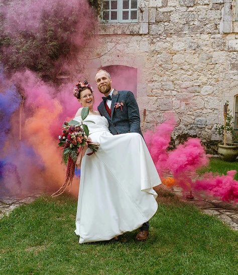 Un couple en tenue de mariage pose devant le château avec des fumigènes lors de leur mariage destination Toulouse Crédit photo : Alex Schmautz