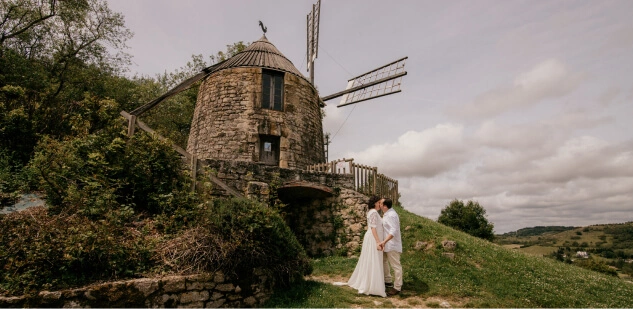 Un couple de mariés s’embrasse devant un moulin dans le Tarn Crédit photo : Sophie Bachère