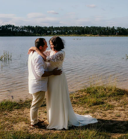 Un couple en tenue de mariage est enlacé devant un lac en Occitanie. Crédit photo : Sophie Bachère